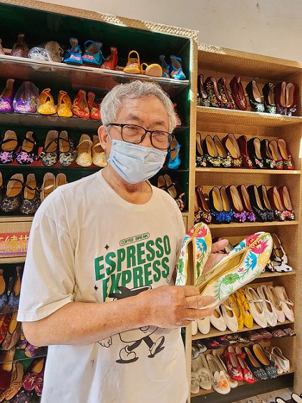 李東志手上拿著為臺南市正覺寺法會設計的繡花鞋，鞋面上的蓮花刺繡象徵「步步生蓮」。（鄭佩雯拍攝）