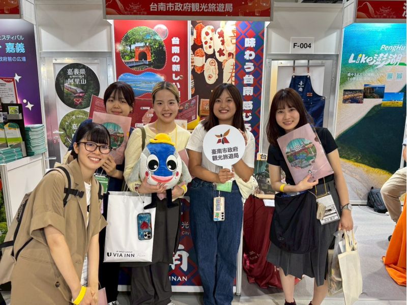 日本旅展現場，參觀民眾與臺南市政府觀光旅遊局文宣品及展物合影，展現對臺南觀光的熱情支持.